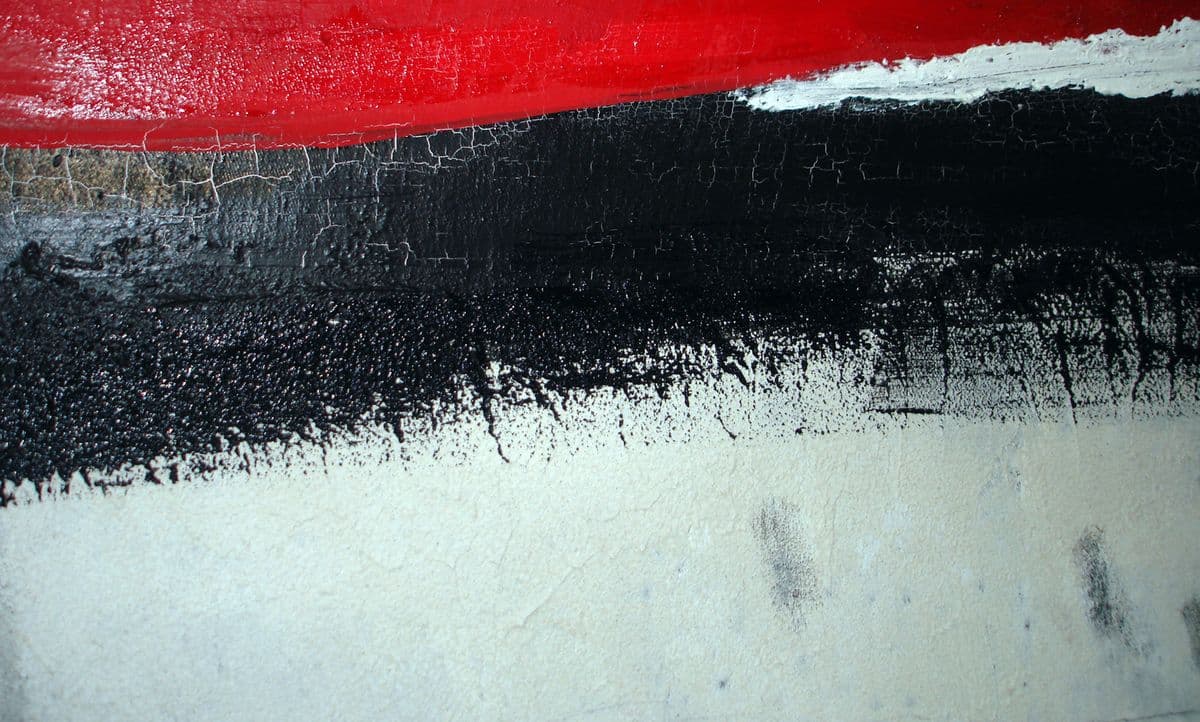 Detailaufnahme einer Malerei mit starker Textur. Horizontale Schichten aus leuchtendem Rot, tiefem Schwarz mit feinen Trocknungsrissen und einem rauen, hellen Untergrund bilden einen starken Kontrast.