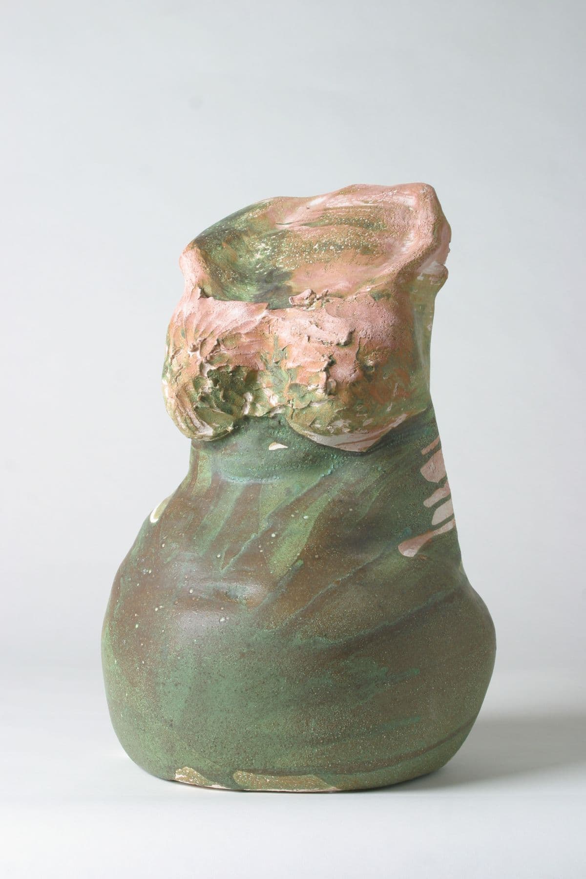 Abstrakte Keramikskulptur eines weiblichen Torsos. Matte, gesprenkelte Glasur in Grün- und Brauntönen, die nach oben hin in unregelmäßige rosa-rosa Bereiche übergeht.