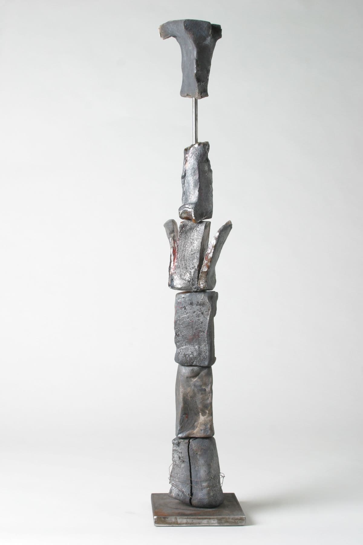 Schlanke, säulenartige Skulptur auf Metallstab mit unregelmäßiger Oberfläche.