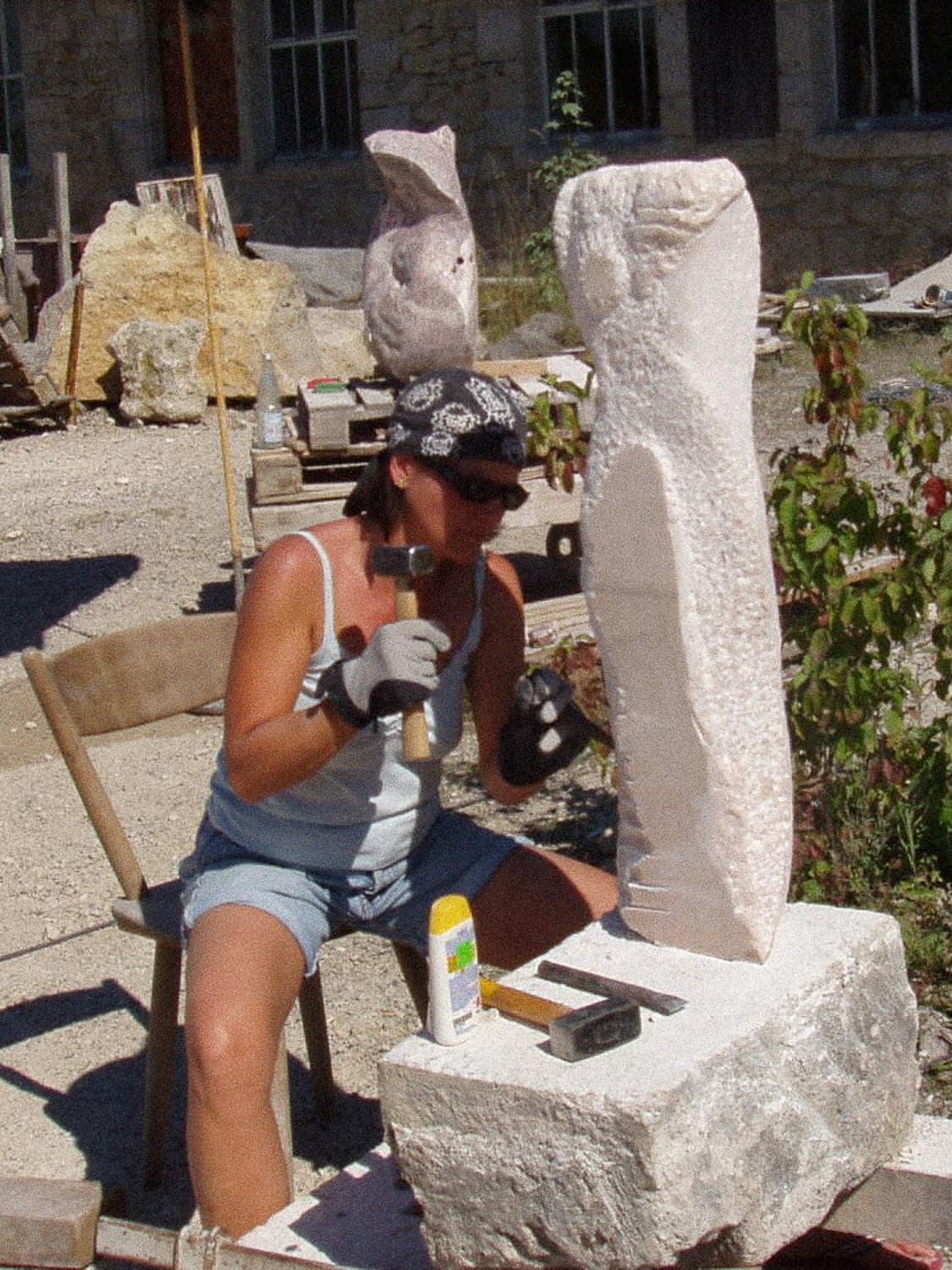 Eine Bildhauerin bei der Bearbeitung einer Steinskulptur mit Hammer und Meißel in einem Außenatelier